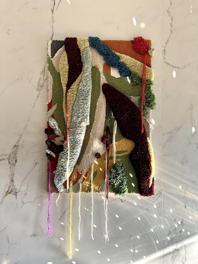 What Remains hand-tufted wall rug made from reclaimed waste yarn, featuring layered abstract textures and hanging yarn details.