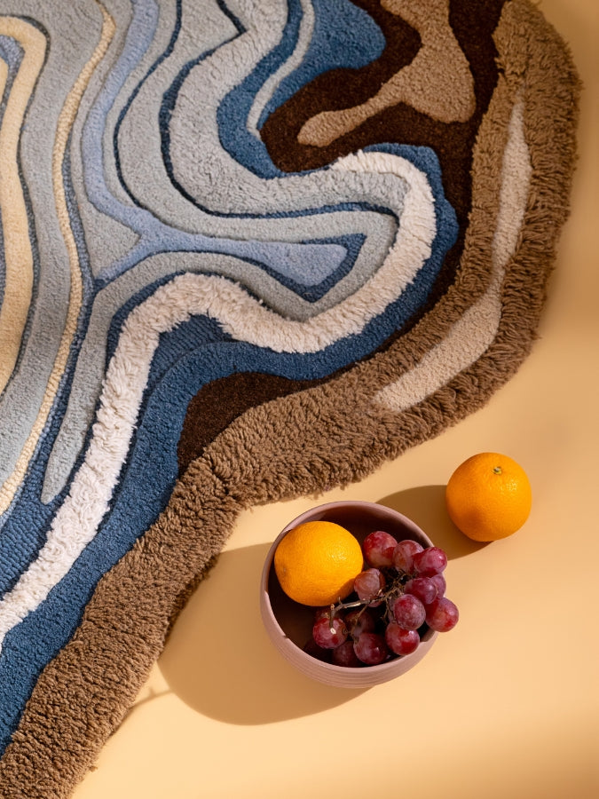 Ocean Eye textured rug featuring layered blue, cream, and sandy brown tones inspired by ocean currents and agate stones.