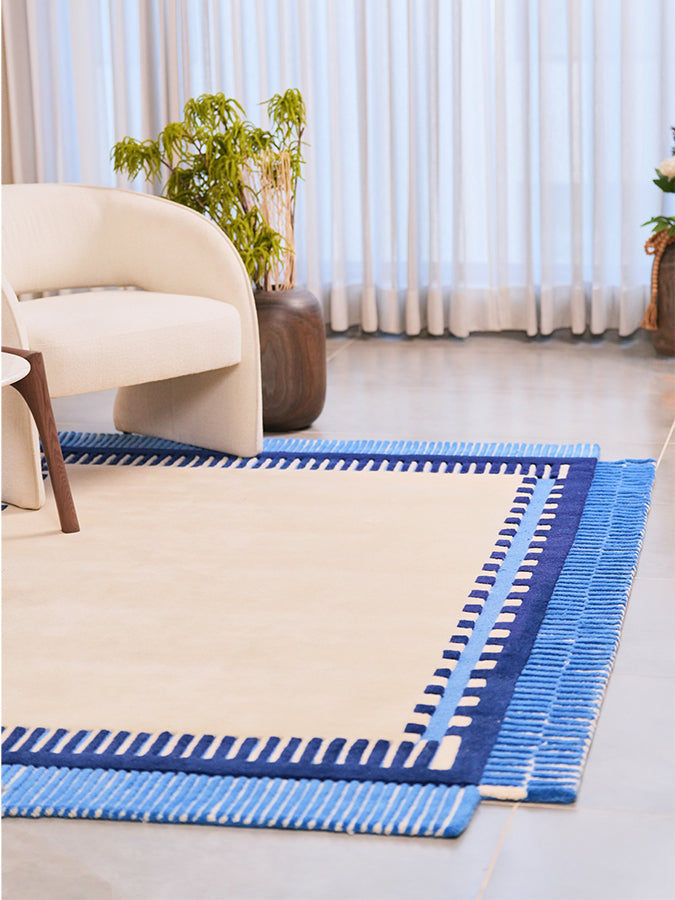 Nested wool and Tencel area rug styled beside a cream armchair, with an ivory centre and blue borders