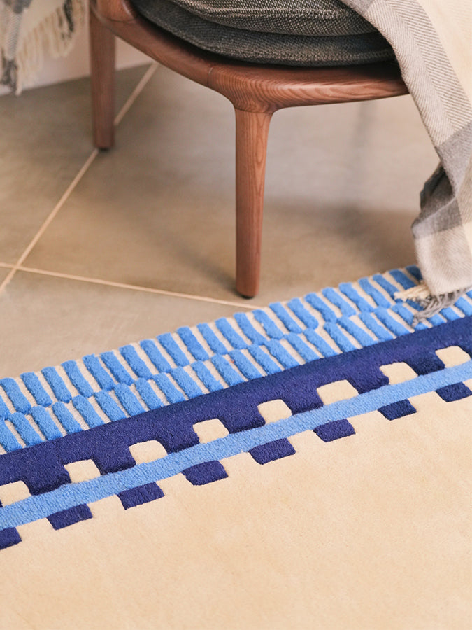 Close-up of Nested hand tufted rug's blue and ivory striped edge beside a wooden accent chair