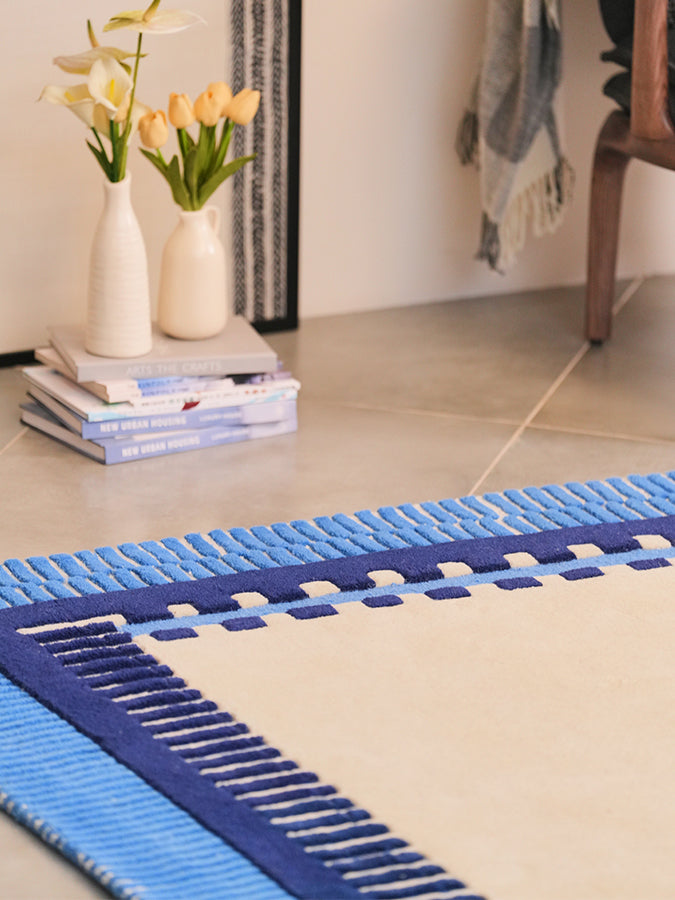 Angled corner of Nested geometric rug showing layered navy and sky blue borders around an ivory centre